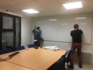 Guillaume et Rodrigue accrochant le tableau blanc au mur de la salle de réunion